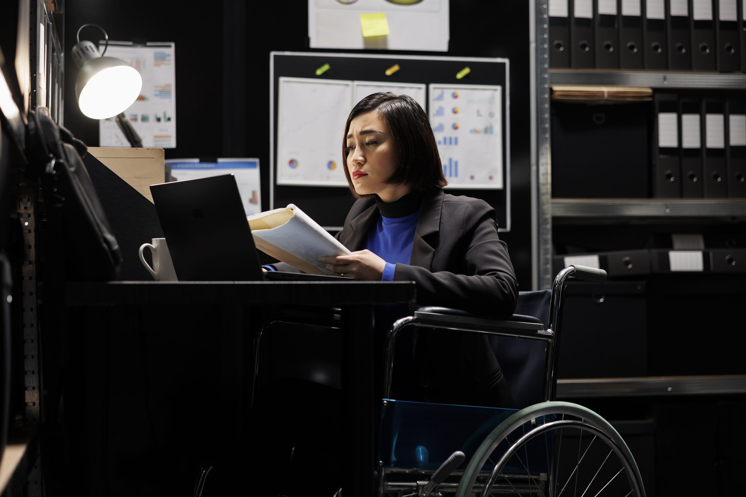 Accountant in wheelchair checking profit Asian accountant in wheelchair checking annual profit revenue documents before business consulting meeting. Woman with paraplegia in bureaucratic workplace filled with flowcharts and folders