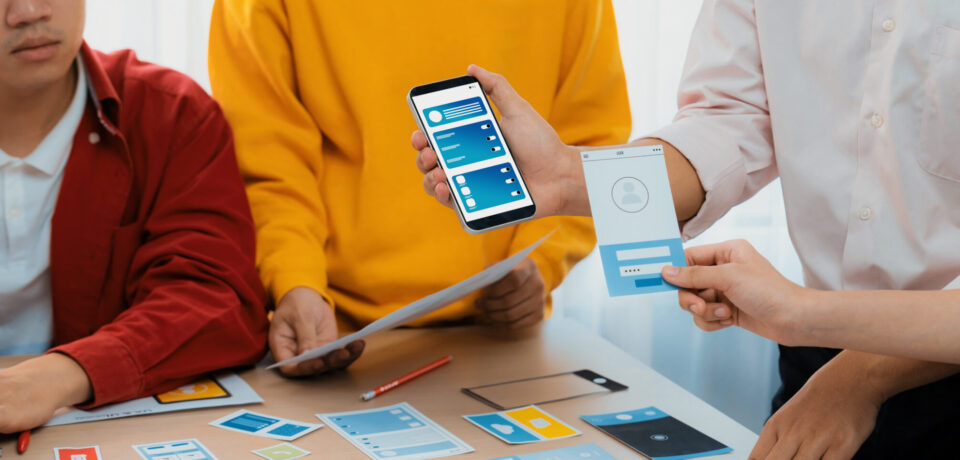 Panorama banner of startup UX developer or company employee design user interface or UI prototype for mobile application or website software with software display on smartphone in office. Synergic